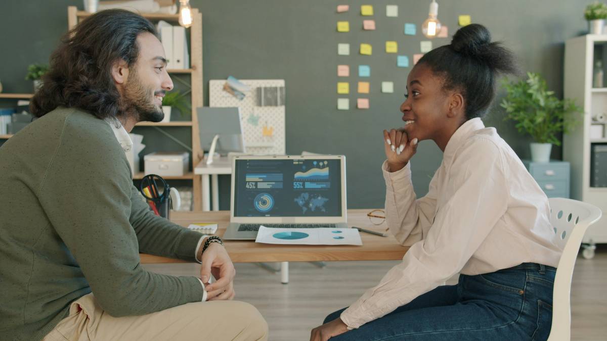 Arab guy and Afro-American girl are chatting and laughing looking at laptop screen in office. Modern technology, teamwork and workplace concept.